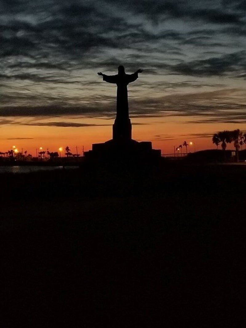 A statue of jesus is silhouetted against a sunset sky.