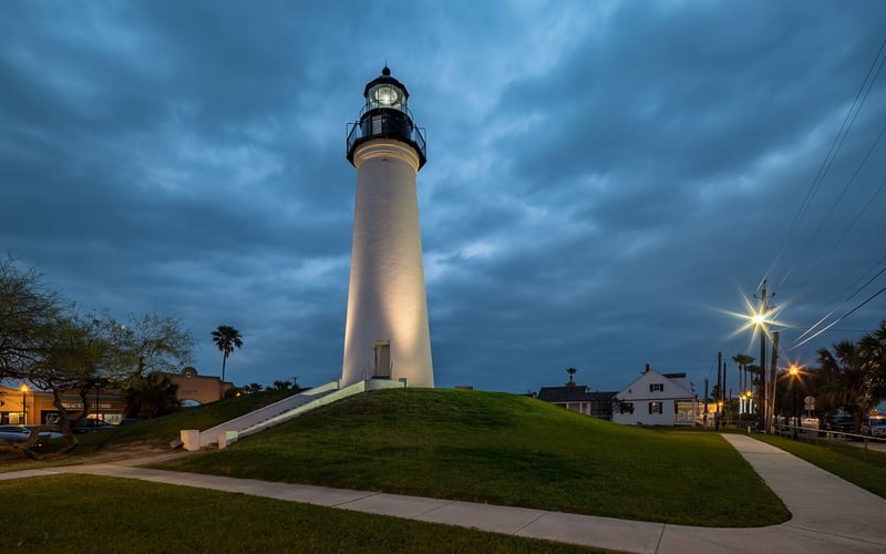 A lighthouse is lit up at night on top of a grassy hill.