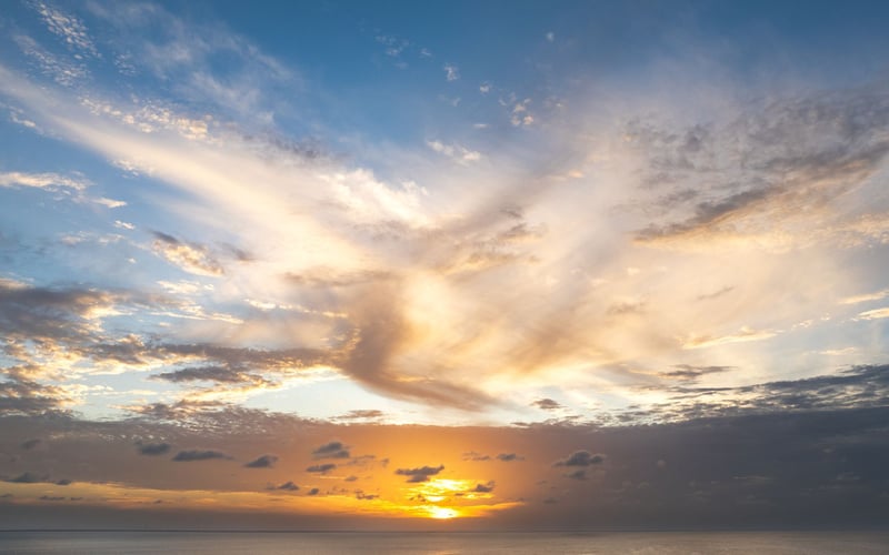 The sun is setting over the ocean with clouds in the sky.
