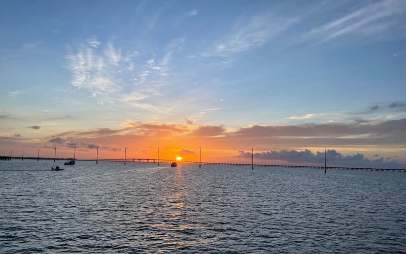 A sunset over a large body of water with a bridge in the distance.