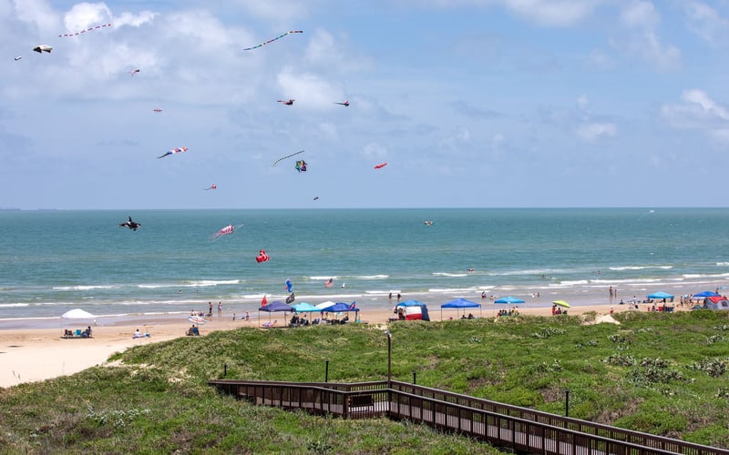 A boardwalk leading to a beach with kites flying in the sky