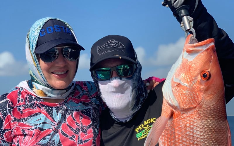 A man and a woman are standing next to each other holding a large red fish.