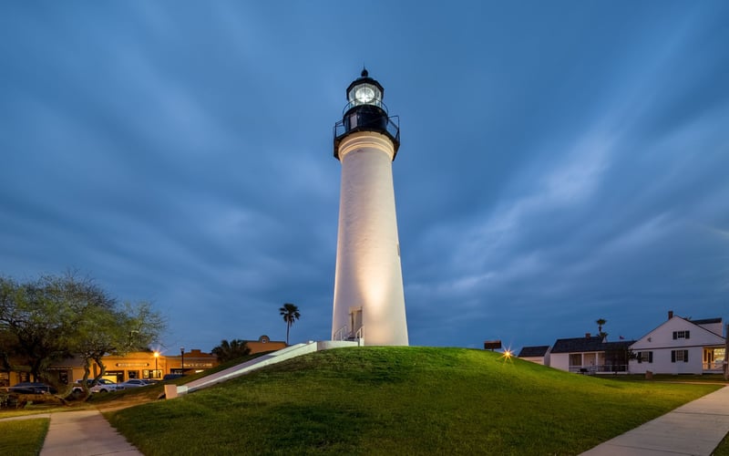 A lighthouse is sitting on top of a grassy hill.