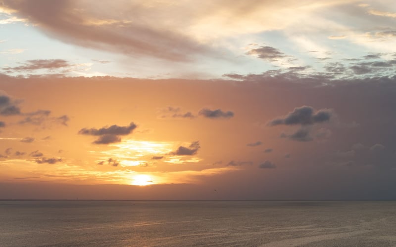 A sunset over the ocean with clouds in the sky