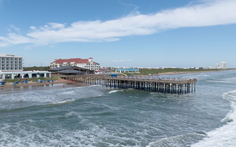An aerial view of a pier in the ocean with a hotel in the background.